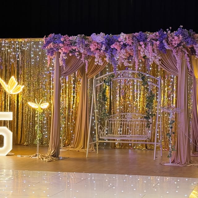 Quinceañera stage with gold sequin backdrop, florals and butterflies by Home Chef UK